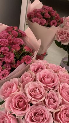 many pink roses are in vases on a table with other flowers behind them,