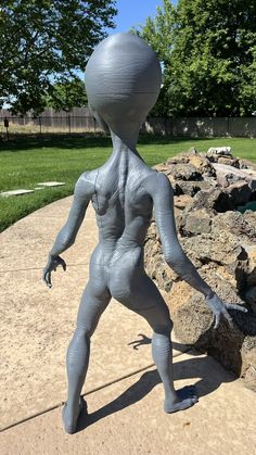 a statue of an alien standing in front of some rocks