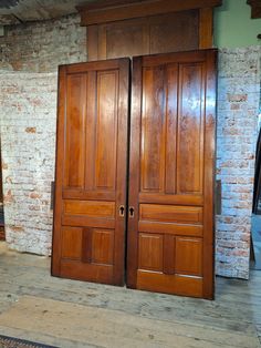 two large wooden doors in front of a brick wall and doormat on the floor