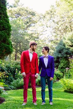 two men in colorful suits standing next to each other on green grass with trees and bushes behind them