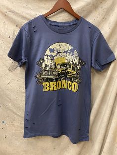 Country Deep Bronco 80's Vintage unisex distressed T shirt in vintage Faded navy 40 Singles Jersey 100% Cotton Premium quality ringspun and compacted cotton Fine Cotton Jersey that is pigment dyed for a more vintage look Features tears and destroyed features at neck and on body Each piece is unique as this process is done by hand! 3.8 oz Made In USA Every garment dye item can be a slightly different shade in color and distressed since this is a laundry dye hand process. Enjoy its unique quality! Medium Fade, Distressed T Shirt, Vintage Look, Vintage Tshirts, Vintage Looks, Premium Quality, Size Chart, Dye, Navy