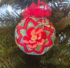 an ornament hanging from a christmas tree decorated with red and green fabric flowers