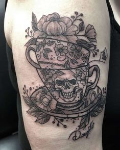 a skull in a cup with flowers and leaves on the side of a woman's thigh