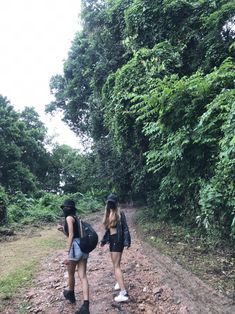 two young women walking down a dirt road in the woods with backpacks on their backs