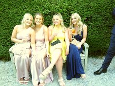 four beautiful women sitting next to each other on a bench in front of a hedge