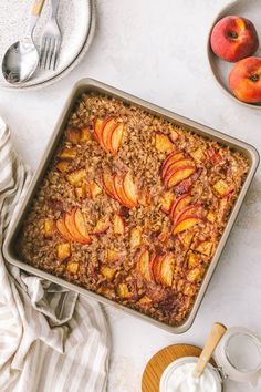 baked oatmeal with sliced peaches in a baking pan next to two plates and spoons