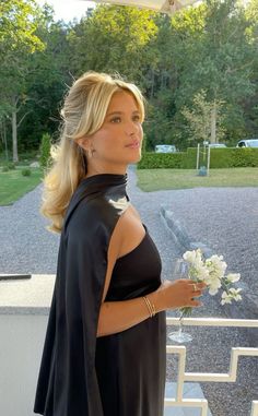 a woman in a black dress holding a bouquet of flowers and looking off into the distance