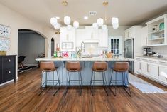 a large kitchen with white cabinets and wooden flooring, along with bar stools