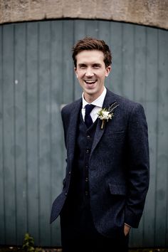 a young man in a suit and tie standing next to a green wall smiling at the camera