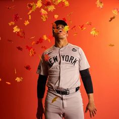 a man in a new york baseball uniform with fall leaves falling from the sky behind him