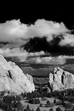 a black and white photo of rocks in the desert under a cloudy sky with clouds