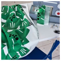 a sewing machine and green fabric on top of a white table with blue chair legs