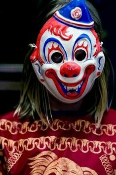 a person wearing a clown mask with long hair and blue eyes is looking at the camera