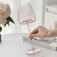 a hand holding a wine glass on top of a table next to a vase with flowers