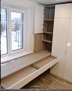 an empty room with white cupboards and wooden flooring next to a large window