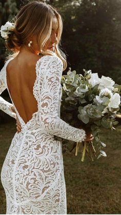 a woman in a white lace dress holding flowers and looking at the back of her dress