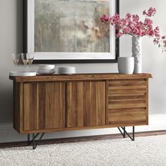 a wooden sideboard with two vases and flowers on it in front of a painting