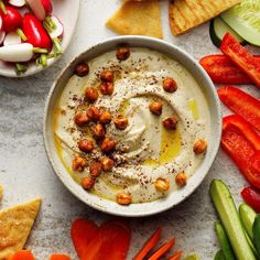 a white bowl filled with hummus surrounded by vegetables and crackers