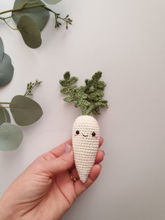 a hand holding a tiny crocheted vegetable with leaves on the side and another plant in the background