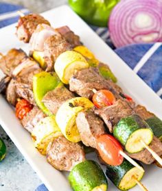 a white plate topped with meat and veggies on skewers next to green peppers