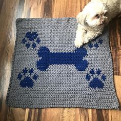 a white dog laying on top of a blue crocheted rug with paw prints