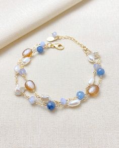 This beautiful layered bracelet showcases a stunning mix of blue and copper gems. The bold mix of gems creates a unique and eye-catching design, while the addition of smooth and baroque pearls adds a touch of elegance. With an adjustable lobster clasp and extender chain, this bracelet offers a perfect fit for anyone looking to make a statement.  Length: 7 inches plus 1-inch extender Materials: gold fill, kyanite, blue lace agate, cultured freshwater pearls, copper moonstone Gift box included. Blue Moonstone Beaded Bracelets With Gemstone Beads, Handmade Blue Moonstone Beaded Bracelets, Handmade Blue Moonstone Bracelets, Blue Moonstone Jewelry With Stones, Adjustable Blue Pearl Bracelet With Gemstone, Blue Gemstone Pearl Bracelet For Gift, Blue Moonstone Bracelets For Healing, Blue Moonstone Bracelet For Healing, Spiritual Blue Moonstone Bracelets