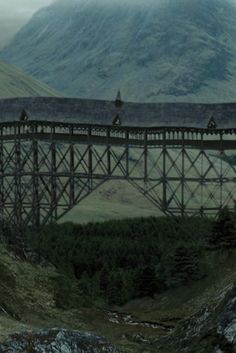 a train crossing over a bridge with mountains in the background and foggy skies above