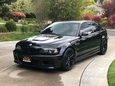 a black car parked on the side of a road next to a lush green park