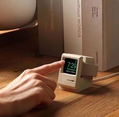 a person pointing at an alarm clock on a wooden table next to some books and boxes