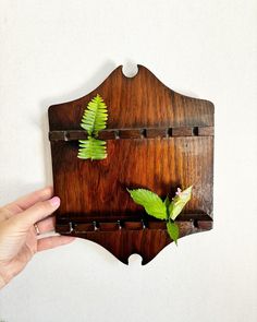 a hand holding a wooden wall hanging with two green leaves on it