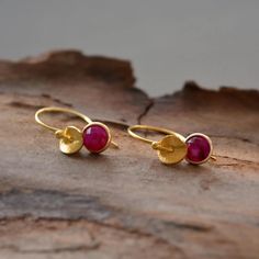 "These beautiful 24k gold vermeil earrings feature a genuine faceted ruby and a twisted textured small disc. Vermeil is a thick coat of 24 karat gold on solid sterling silver. The ruby stone, set in an open-back setting, is suspended from a French style ear wire. Ruby, the king of precious stones, is the birthstone for July, as well as the gemstone of 15th and 40th wedding anniversaries. Ruby is known as the stone of love, passion and romance. It is also believed to bring good luck, prosperity and success. These lovely earrings would make a wonderful gift for yourself or your loved one. Perfect for weddings, bridesmaids gifts, birthday gifts or just a special day out. Comfortable and suitable for everyday wear. They are available in a choice of 8 different gemstones. Please select your sto Gold Faceted Ruby Earrings, Gold Earrings With Ruby Birthstone, Gold Ruby Earrings With Birthstone, Thick Coat, 24 Karat Gold, Birthstone Earrings, Peridot Stone, Ruby Earrings, Ruby Stone