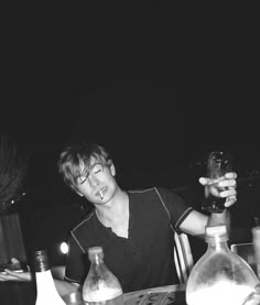 a young man sitting at a table with bottles and glasses in front of his face