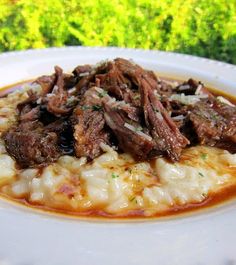 a white plate topped with meat and grits covered in gravy on top of mashed potatoes