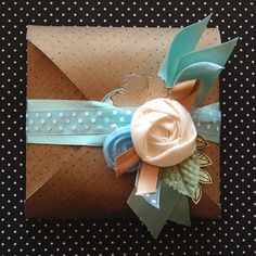 a gift wrapped in brown paper with a blue ribbon and a flower on the top