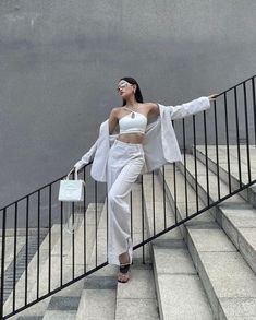 a woman is walking down the stairs with her hand on her hip and wearing white clothing