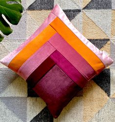 a pink and orange pillow sitting on top of a rug next to a green plant