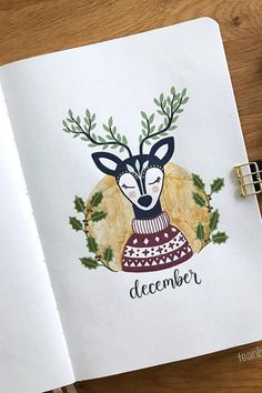 an open notebook with a drawing of a deer wearing a sweater and wreath around its neck