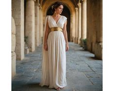 a woman in a long white dress standing on a stone walkway with columns and arches