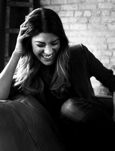 a black and white photo of a smiling woman sitting on a couch with her hand in her hair