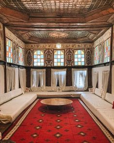 a room with several white couches and a red rug on the floor in front of two windows