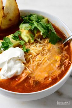 a bowl of soup with sour cream, bread and avocado on the side