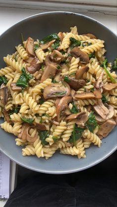 pasta with mushrooms and spinach in a bowl on a table next to a window