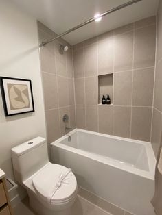 a white toilet sitting next to a bath tub in a bathroom under a framed picture