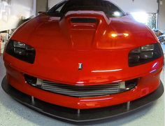 the front end of a red sports car parked in a garage with other cars behind it