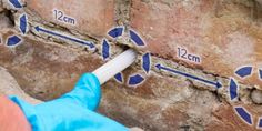 a hand in blue gloves is pointing at a brick wall with two measurements on it