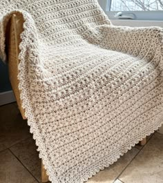 a white crocheted blanket sitting on top of a wooden chair next to a window