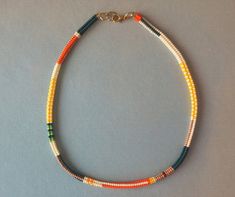 a multicolored beaded necklace is displayed on a gray surface with a gold clasp