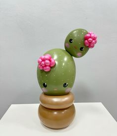 two green cactus with pink flowers on their heads sitting on top of a wooden stand