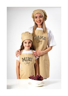 two girls wearing aprons and hats standing next to each other in front of a bowl of grapes