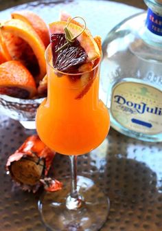 an orange drink with garnishes in a glass on a table next to fruit